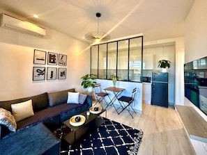 A modern living room with a sofa, coffee table, and chairs, a dining area with a table and chairs, and a kitchen with a refrigerator and microwave.