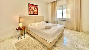 A hotel room with a large bed, a headboard, a bedside table with a lamp, a rug, and a window with curtains. - Elyssa Superbe Appartement aux Jardins de Carthage (Tunis)