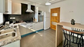 A modern kitchen with white cabinets, a built-in microwave, a double oven, and a gas stove. There is a wooden dining table with chairs and a small vase on the table. - Elyssa Superbe Appartement aux Jardins de Carthage (Tunis)