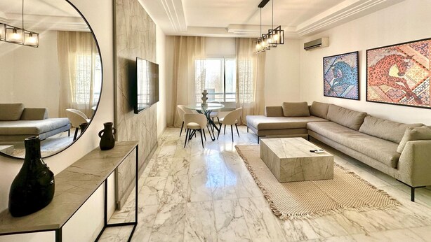 A modern living room with a marble floor, a large round mirror, a sofa, a coffee table, and artwork on the walls. - Elyssa Superbe Appartement aux Jardins de Carthage (Tunis)
