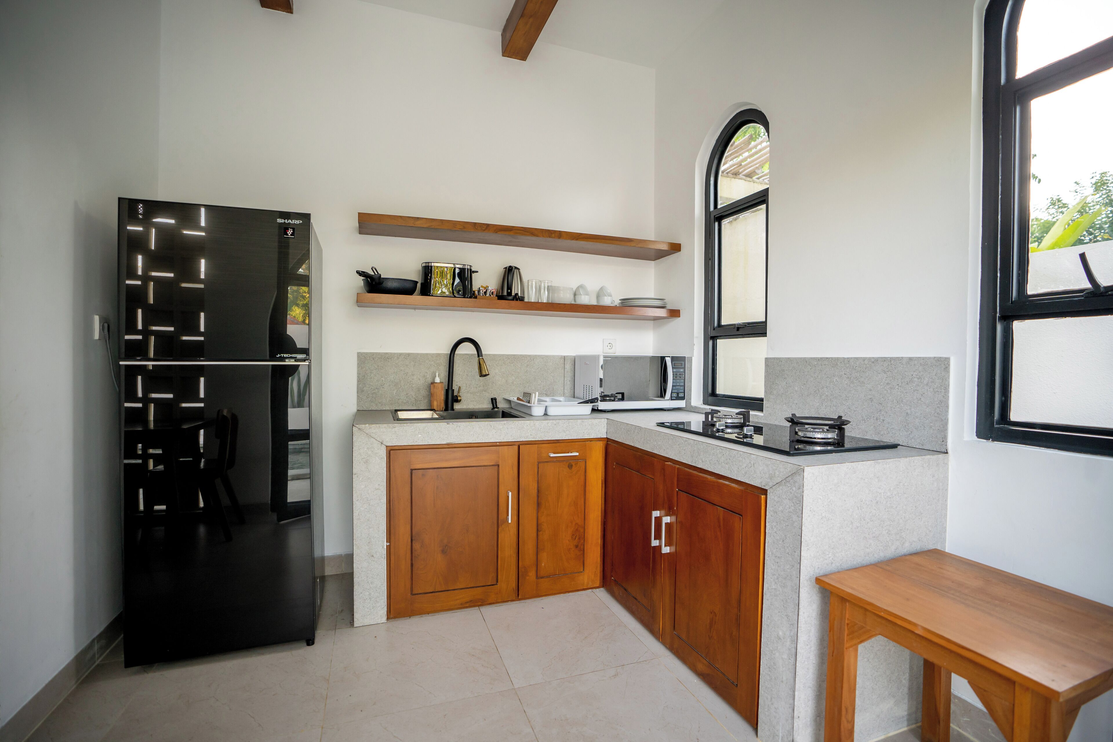A compact kitchen with a black refrigerator, wooden cabinets, a countertop microwave, and a wooden table.