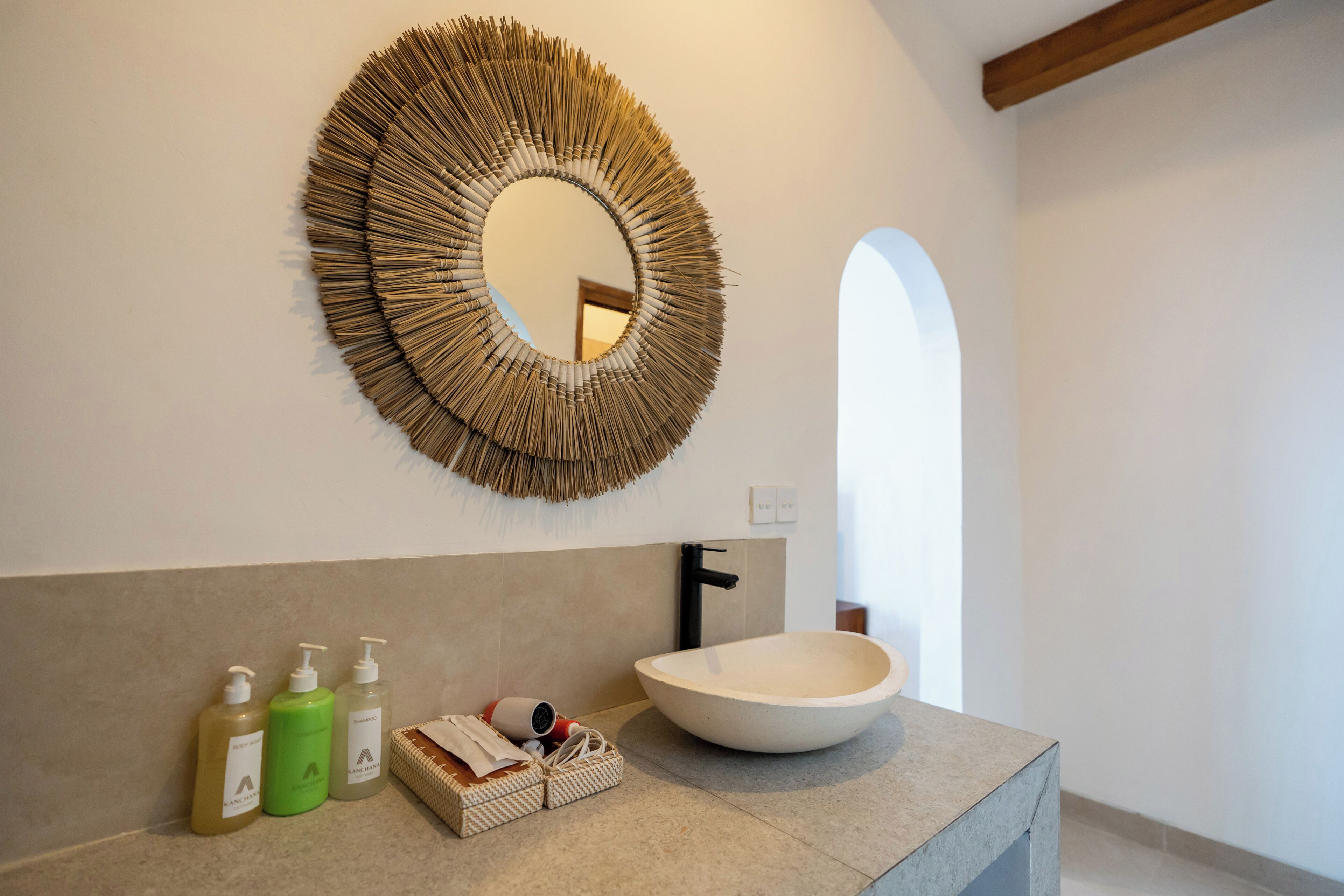 A bathroom with a round mirror, a large sink, and toiletries on the counter.