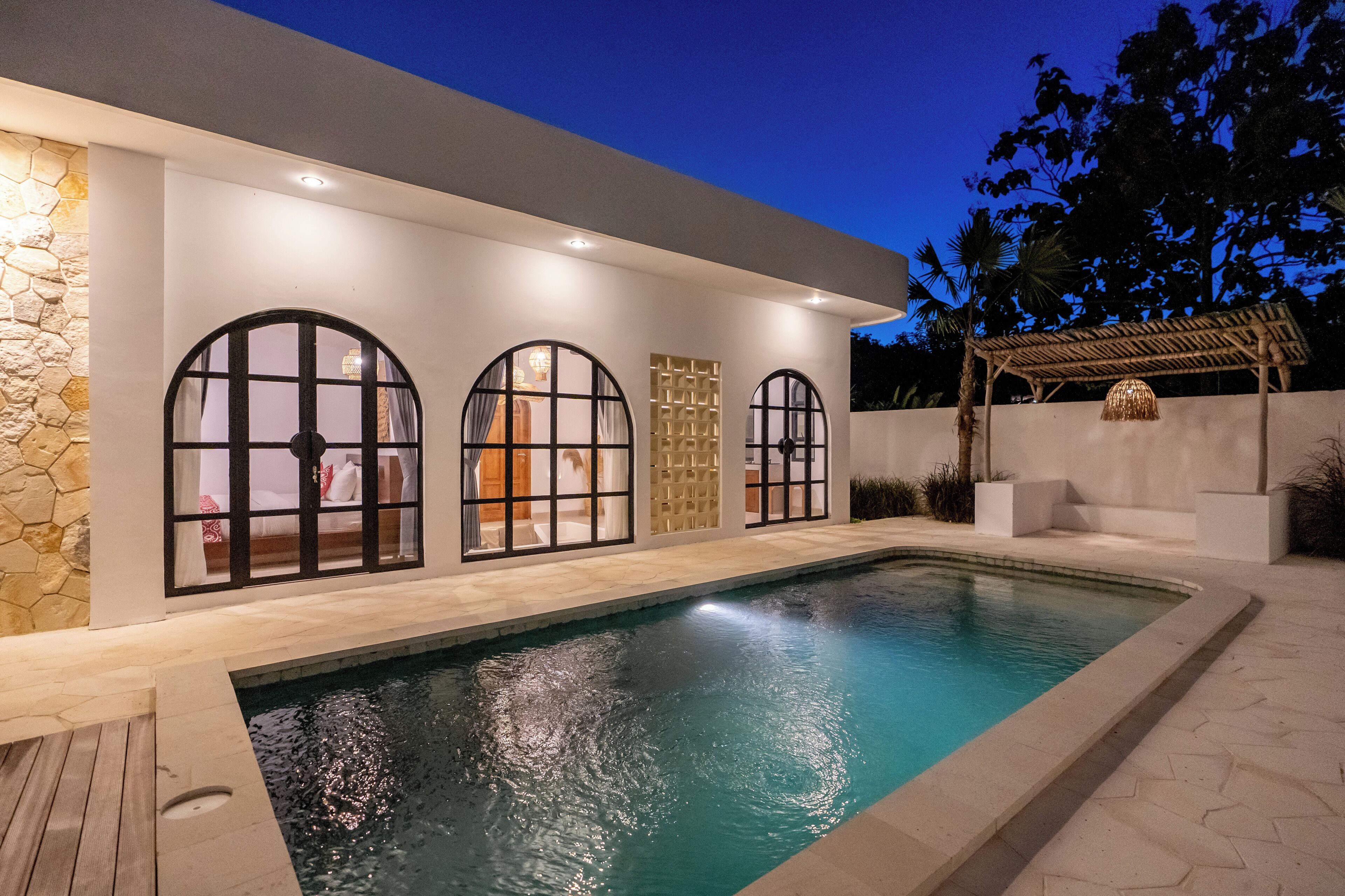 A modern house with a swimming pool, large arched windows, and a stone wall.