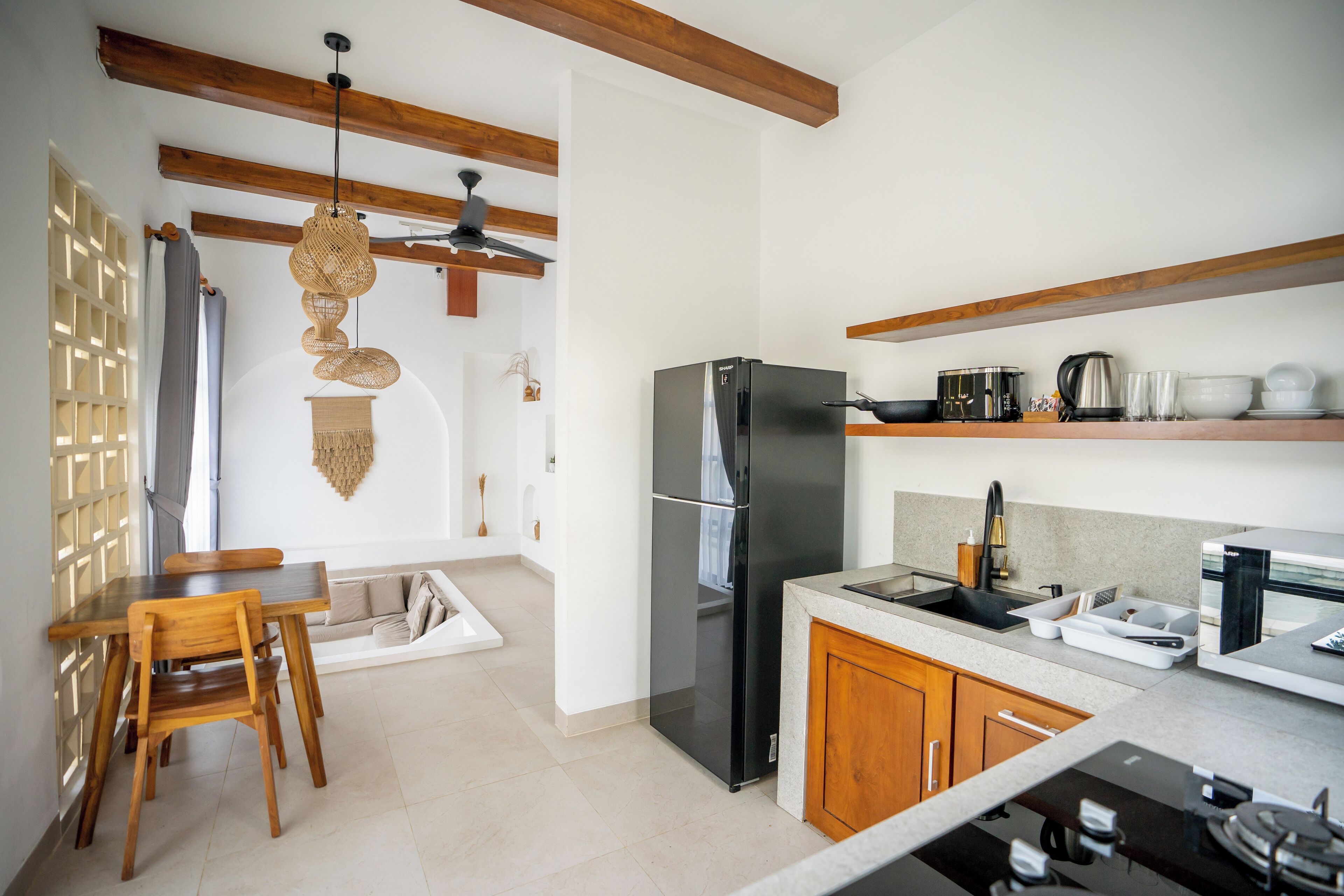 Een moderne keuken met houten balken, een zwarte koelkast, een eethoek met een houten tafel en stoelen, en een klein kookeiland met een spoelbak en aanrecht.