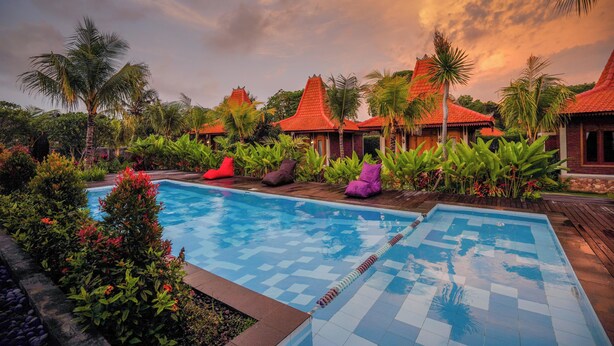 A swimming pool with a checkered pattern, surrounded by lush greenery and palm trees. - Kanchana Cottages (Pecatu)