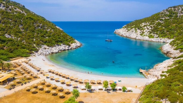 A beach with clear turquoise waters, a small boat, and a row of thatched umbrellas. - Villa Ariadne in Apergatika (Paxos)