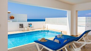 Area piscina con vista sul mare, sedie a sdraio e un tavolo con una bottiglia.