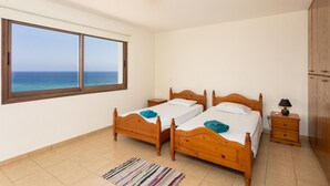 Una camera da letto con due letti in legno, un comodino con una lampada, una finestra vista mare e una luce a soffitto.