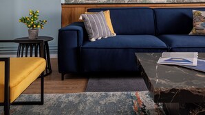 Un salón con un sofá azul, una mesita, una silla y un cuadro abstracto grande en la pared.