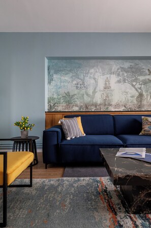 Ein modernes Wohnzimmer mit einem blauen Sofa, einem kleinen Tisch mit einer Pflanze und einem großen abstrakten Gemälde an der Wand.