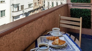 Un balcón con una mesa preparada para dos, dos tazas de café y dos croissants.