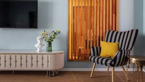 Una sala de estar moderna con un televisor, un busto decorativo, un florero con flores, un sillón a rayas con un cojín amarillo y una partición de listones de madera.