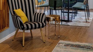 Un comedor con sofá a rayas, una mesa, sillas y piso de madera.