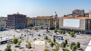 Una plaza urbana con edificios, un anuncio luminoso grande y un autobús.