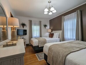 A hotel room with two beds, a television, a desk with a lamp, and a large mirror.