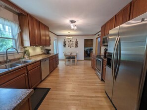 A kitchen with wooden cabinets, a stainless steel refrigerator, a dining table, and a chandelier.