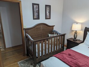 A bedroom with a wooden crib, a bedside table with a lamp, and two framed pictures on the wall. - Harriet House in Potsdam (Potsdam)