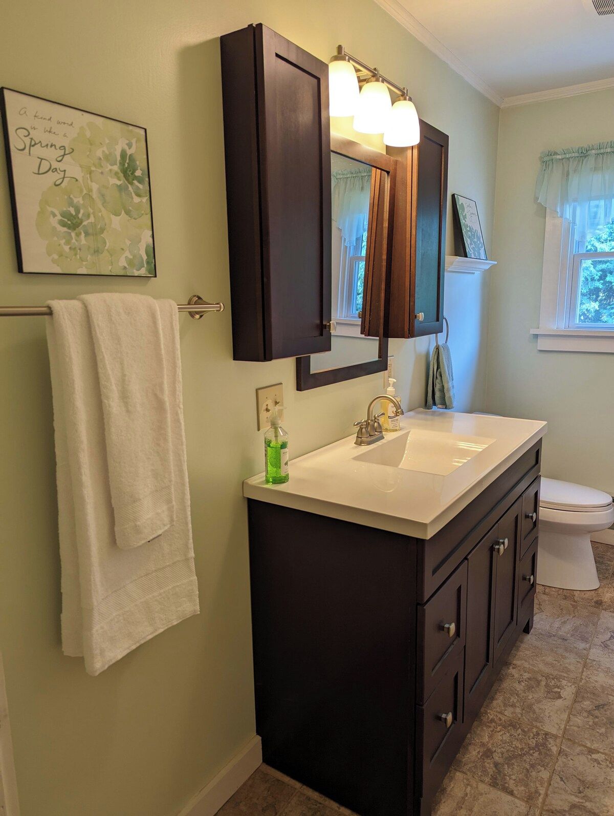 A bathroom with a white sink, dark cabinetry, a mirror with lights, a towel rack, and a framed picture on the wall.