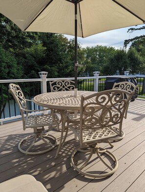 A round outdoor table with four chairs, an umbrella, and a railing on a wooden deck.