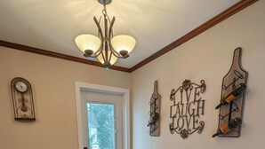 Uma sala de jantar com mesa de madeira, cadeiras brancas, um candelabro e decorações nas paredes.