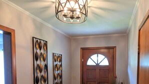 Um corredor com piso de madeira, luminária decorativa e duas obras de arte fixadas na parede.