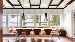 Un comedor con una mesa grande y sillas, ventanas amplias con vistas a un lago y un techo de madera.