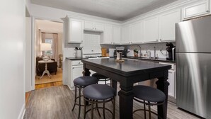 Une cuisine moderne avec des meubles blancs, un réfrigérateur en acier inoxydable et un îlot central doté de tabourets de bar.