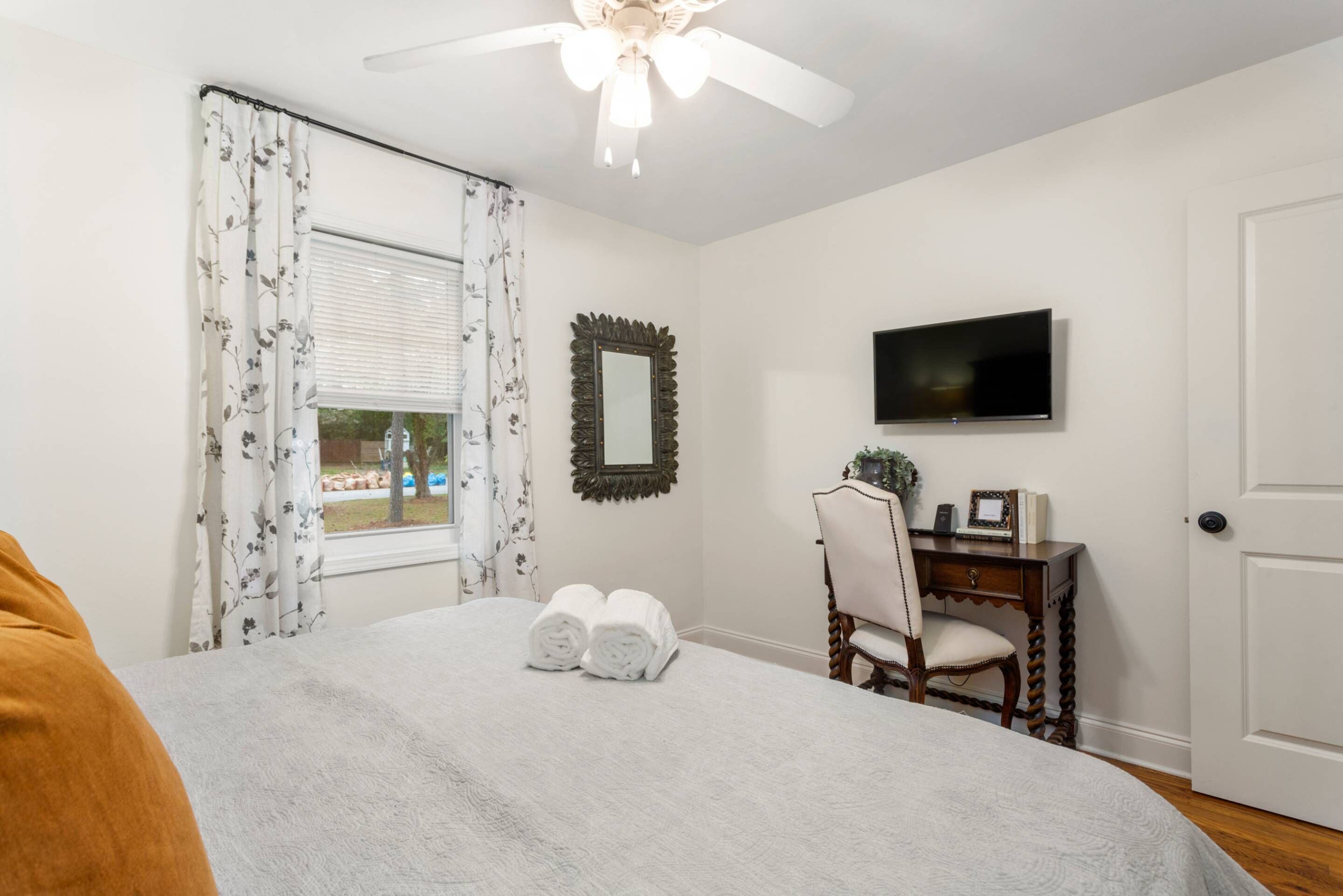 A bedroom with a bed, a desk, a chair, a television, and a door.