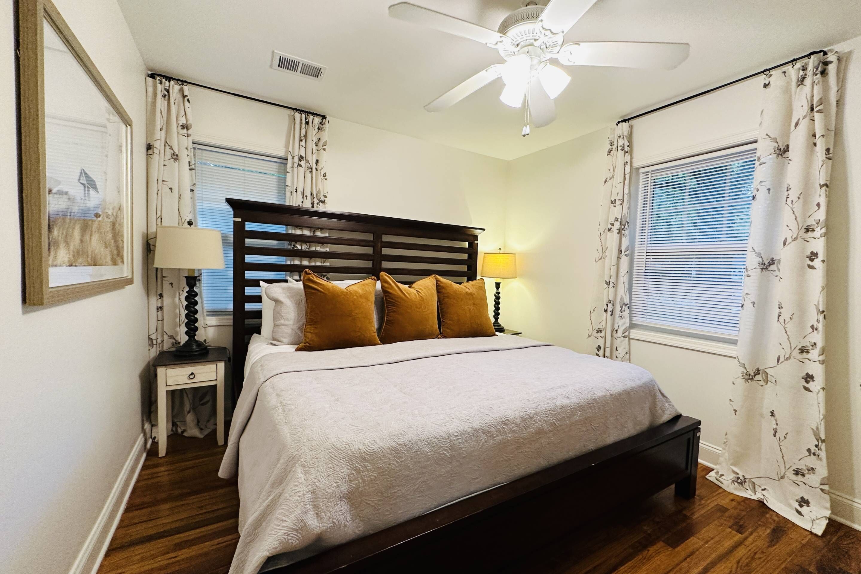 A neatly arranged bedroom with a bed, bedside lamps, a ceiling fan, and curtains.