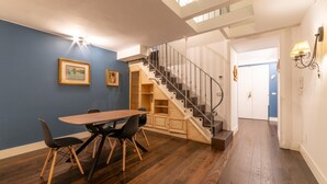 Un comedor con una mesa y sillas de madera, una escalera y una puerta que da a otra habitación.