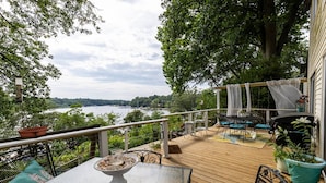 Une terrasse en bois avec des meubles d’extérieur, une table à manger avec un saladier, et une vue sur un lac.