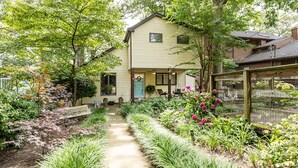 Une maison avec un chemin de jardin menant à la porte d’entrée, entourée de différentes plantes et fleurs.