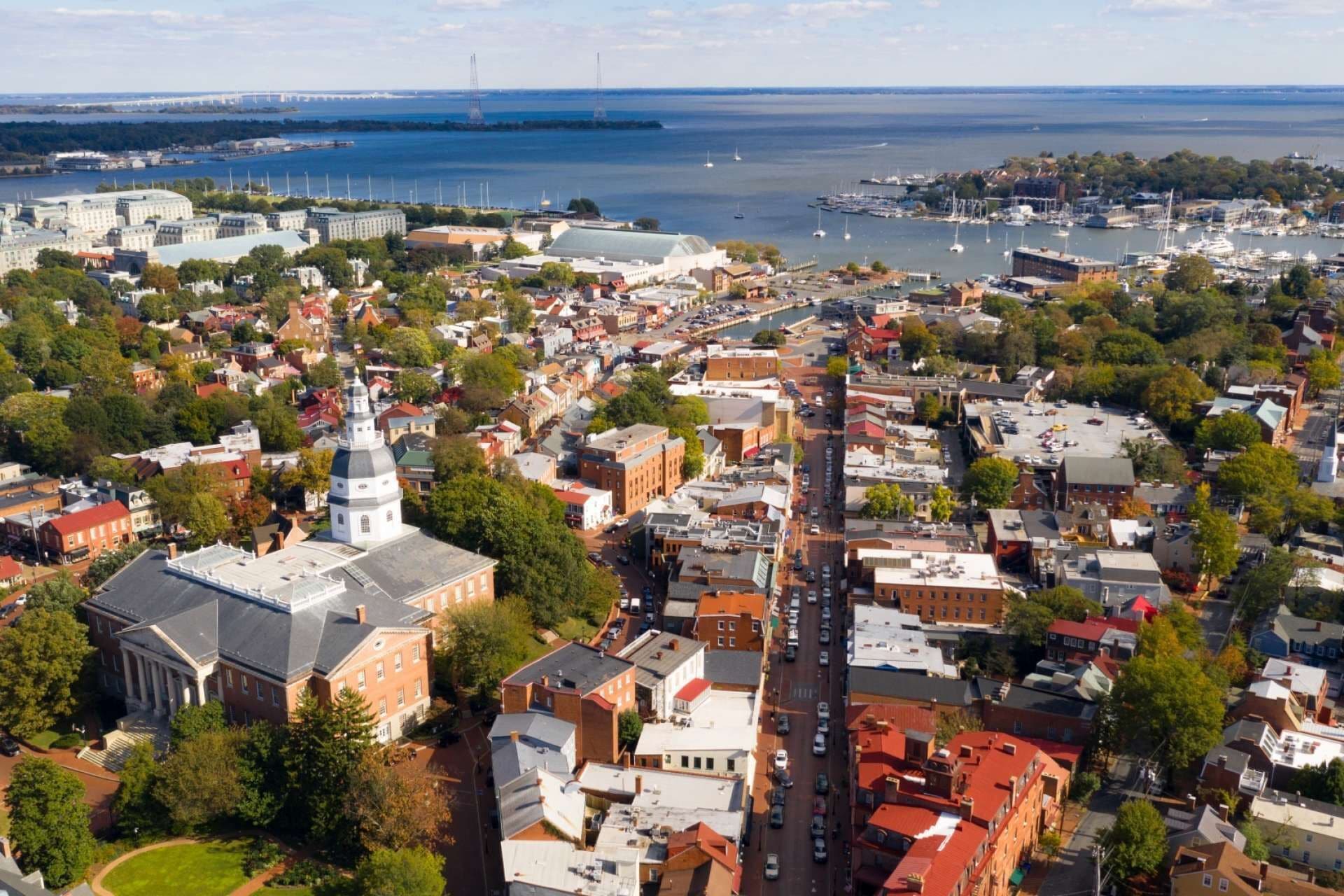 An aerial view of a coastal town with a prominent church, a marina, and a bridge in the background.