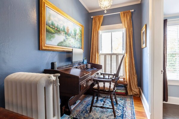 A room with a desk, chair, radiator, and a window with curtains.