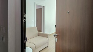 En öppen dörr leder in till ett rum med en beige soffa, ett trägolv och en luftkonditioneringsanläggning på väggen.