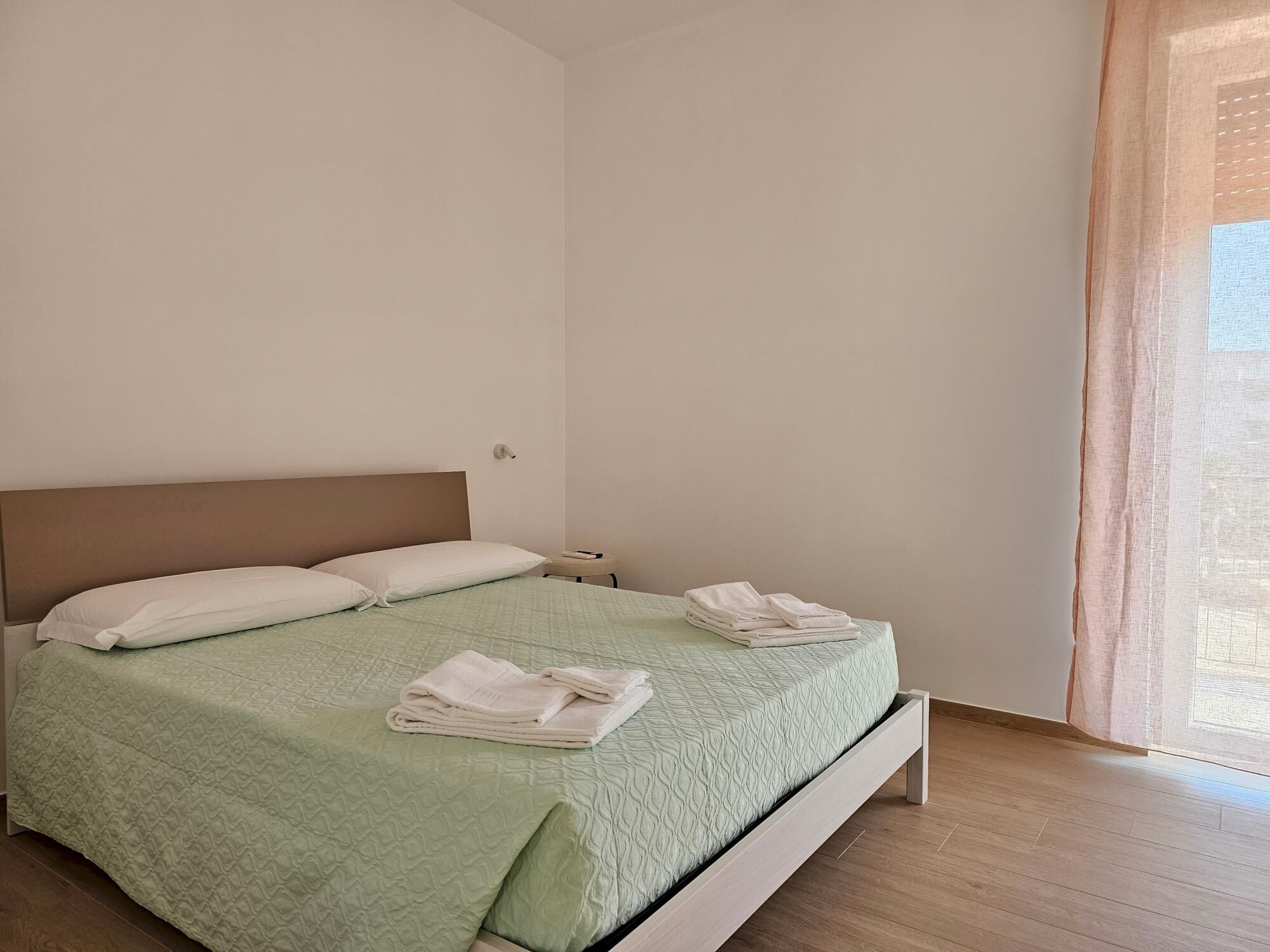 Ein ordentlich gemachtes Bett mit einer grünen Decke, zwei Kissen und gefalteten Handtüchern daneben.