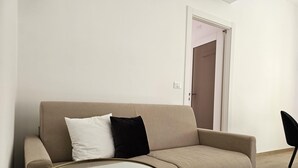 En beige soffa med två kuddar, ett litet runt bord och en dörr i bakgrunden.