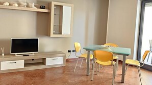 A modern living room with a flat-screen TV, wooden entertainment unit, and a dining area with yellow chairs. - Casa Calette in Monopoli (Monopoli)
