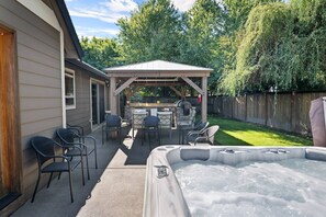 A backyard with a hot tub, patio furniture, and a barbecue area.