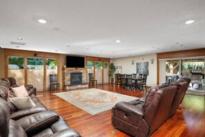 A spacious living room with a fireplace, leather sofas, a dining area, and a view through large windows.