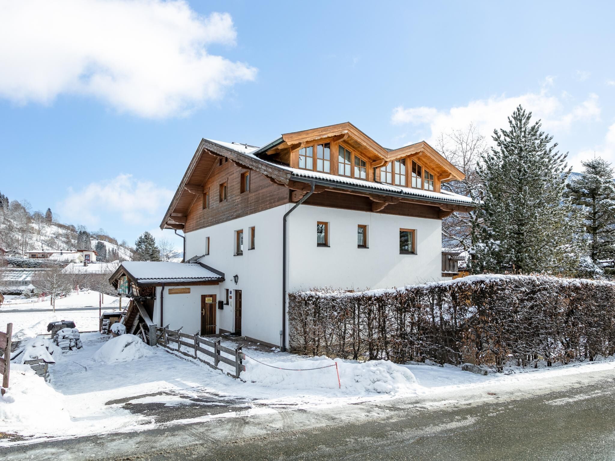 En toetagers chalet med træfacade og skråt tag, omgivet af snedækkede arealer og træer.