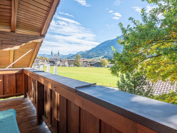 A wooden balcony with a view of a village, mountains, and a church.