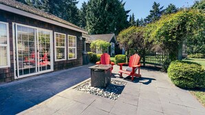 A patio with a fire pit and Adirondack chairs, surrounded by a stone pathway and a wooden fence. - Sit Back & Watch Waves at Rathtrevor Cottage (Parksville)