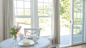A dining table set for two with white plates, cups, and cutlery, positioned near a window with curtains. - Sit Back & Watch Waves at Rathtrevor Cottage (Parksville)