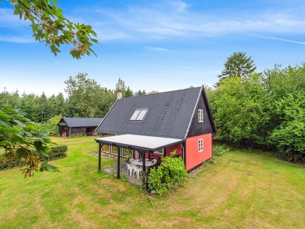 Une maison rouge avec un toit noir, une véranda et un petit jardin.