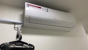 Eine weiße Klimaanlage an der Wand montiert, mit einem weißen Schlauch und einem schwarzen Haken.