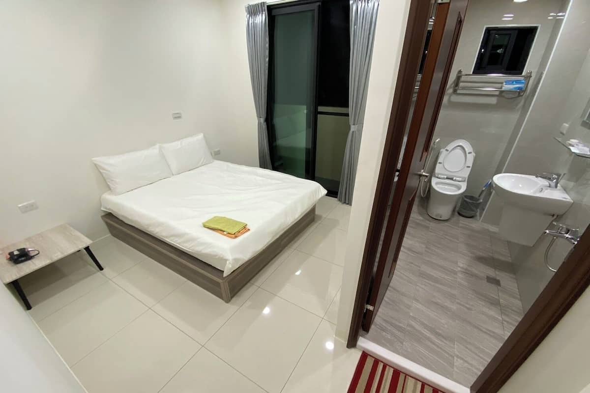 Une chambre d’hôtel comprenant un lit, une petite table de chevet et une salle de bain avec des toilettes, un lavabo et une douche.