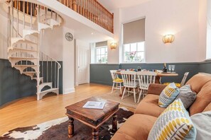 Una habitación amplia con una escalera de madera, un comedor con mesa y sillas, y un sofá de cuero con cojines estampados.