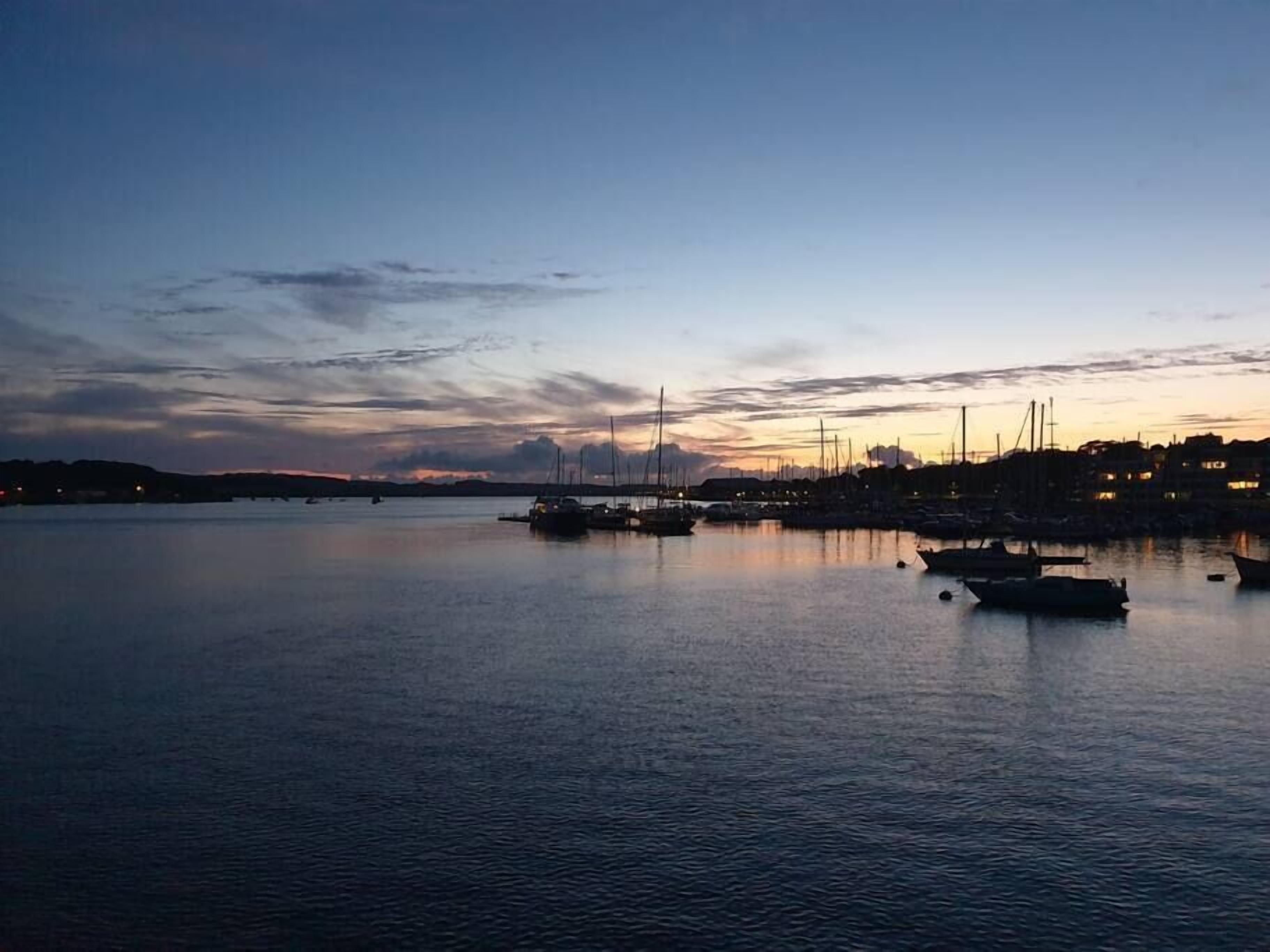 Un rivage paisible, avec des bateaux et, au loin, la silhouette d’une ville.