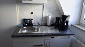 Une cuisine compacte équipée d’un évier, d’une machine à café et d’un égouttoir à vaisselle.